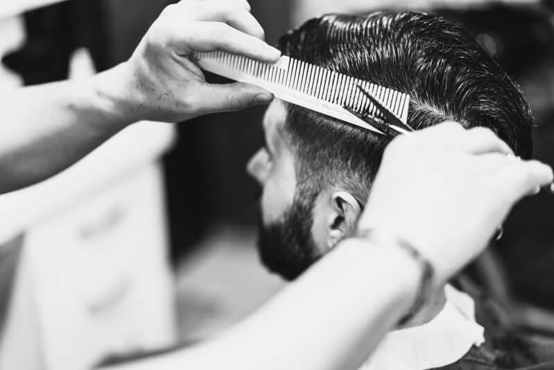 Barber styling a men's haircut with comb and scissors