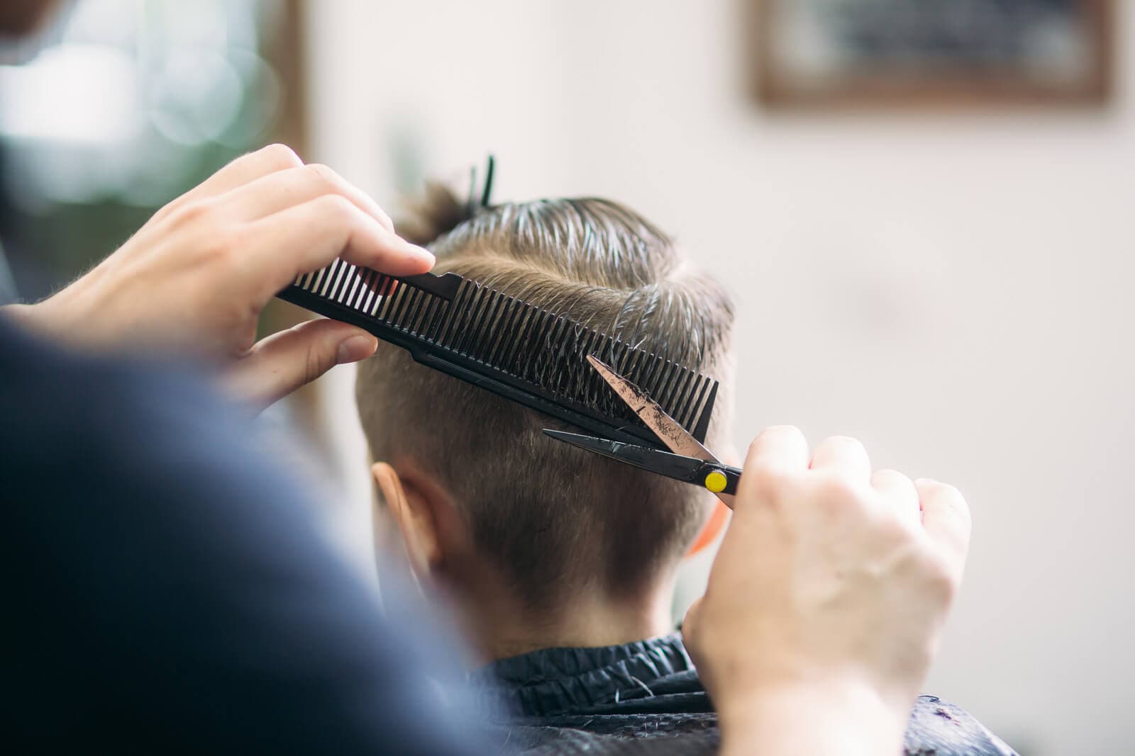 Hairdresser cutting the top of a haircut with comb and scissors