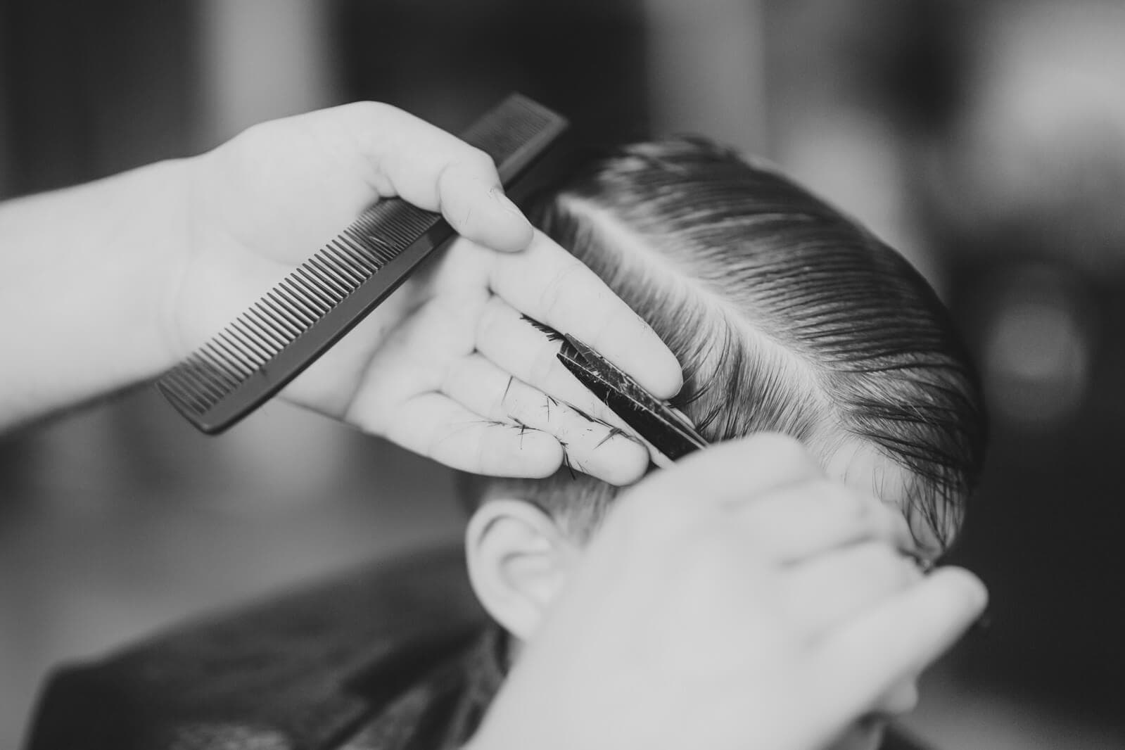 Barber cutting a side-parted haircut with comb and scissors